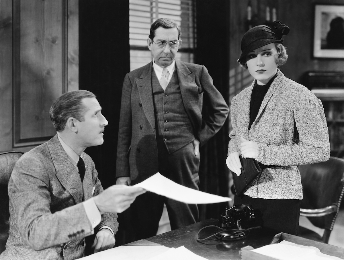 Three people exchanging a document at a desk with a rotary telephone